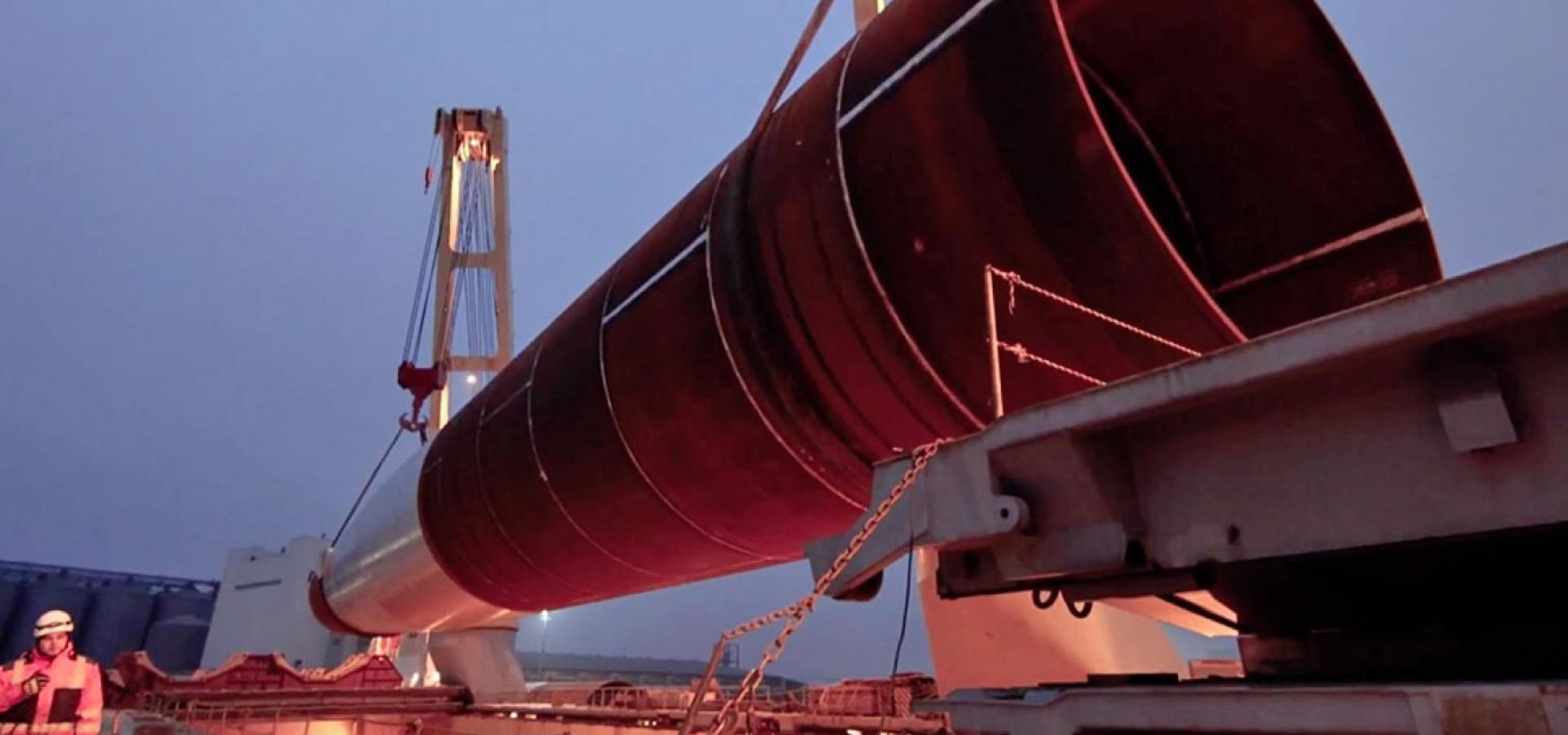 Large industrial cylinder being lifted by a crane at dusk