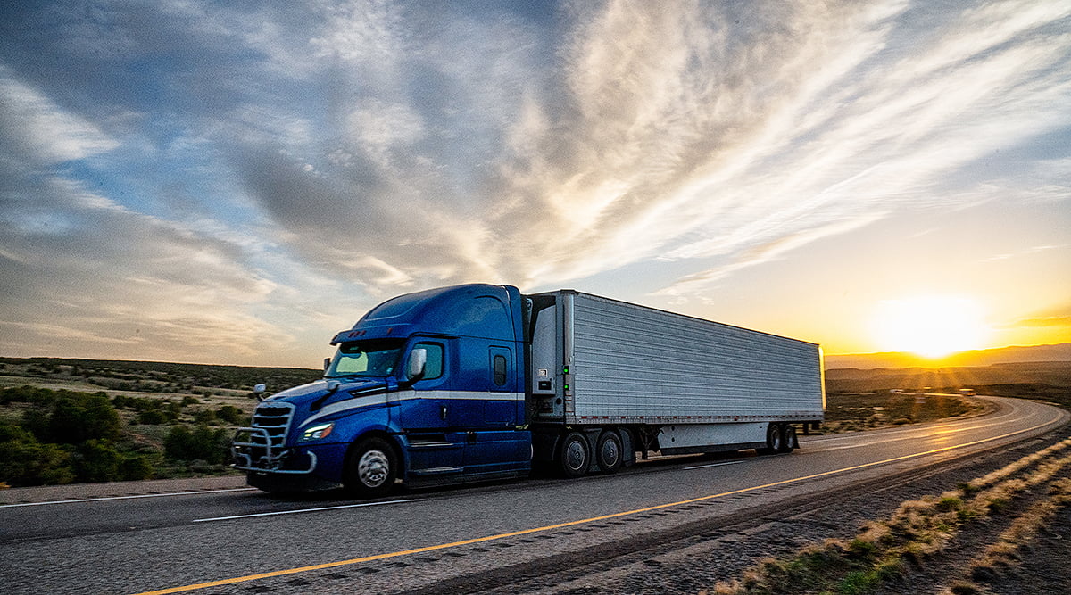 Truck hauling a trailer on an open highway at sunset